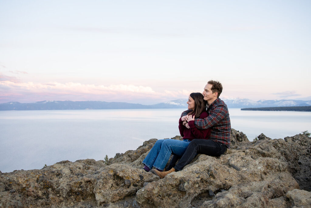 the couple sits side by side on rocks, arms wrapped around each other in a peaceful and intimate embrace during their Eagle Rock engagement photos