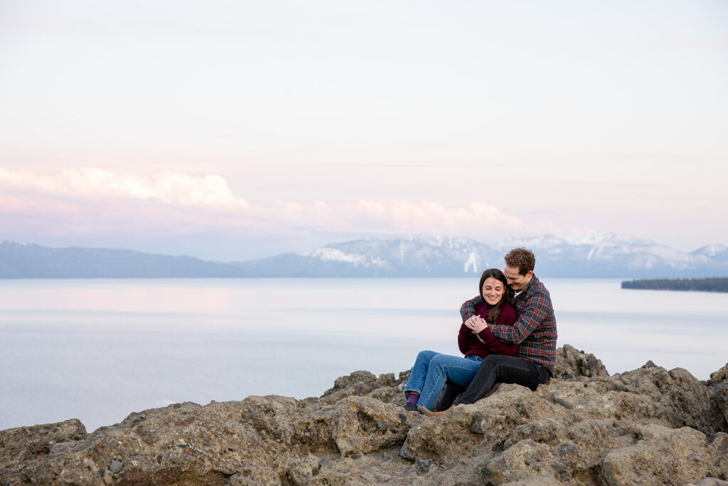 the couple sits side by side on rocks, arms wrapped around each other in a peaceful and intimate embrace during their Eagle Rock engagement photos