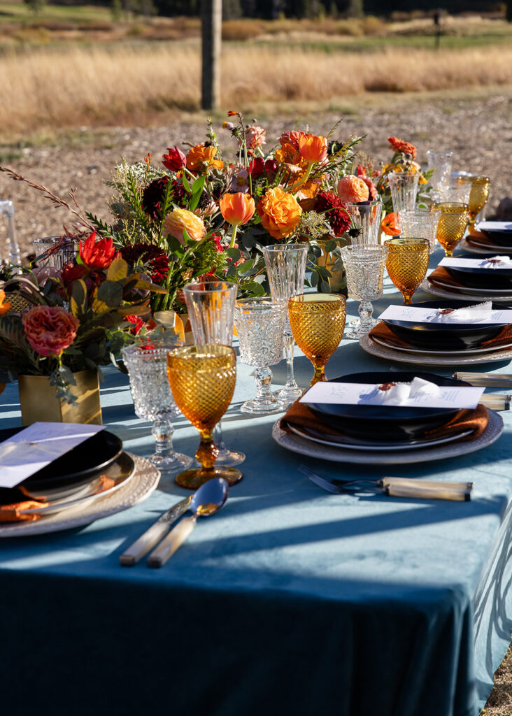 Side view of the colorful wedding table setup at Olympic Valley Stables with bold florals and vintage glassware