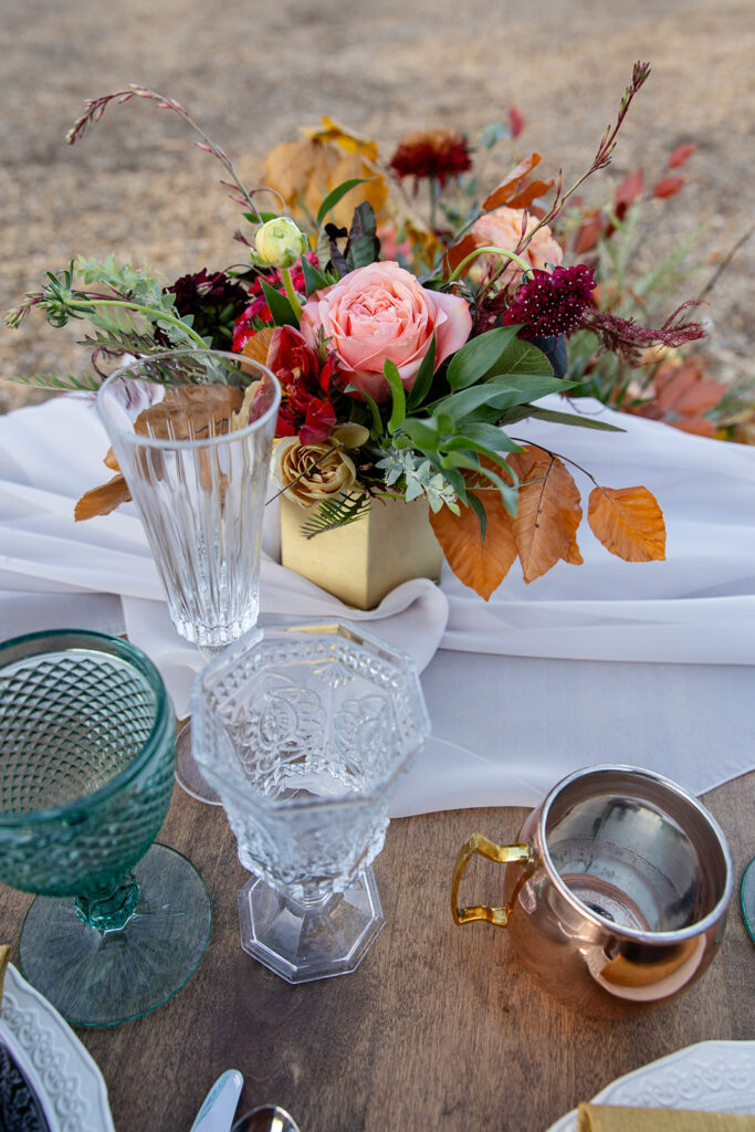 Romantic sweetheart table with an ivory settee and a cascade of orange, pink, and burgundy flowers on flowing white fabric, set in a mountain meadow at Olympic Valley Stables
