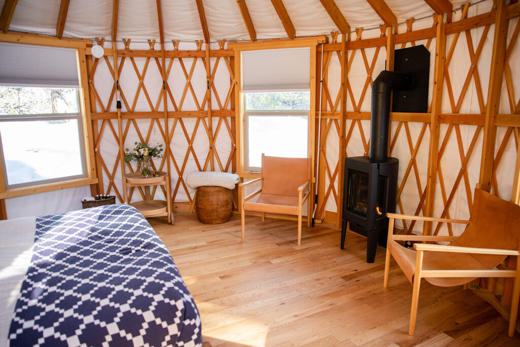 Warm, rustic yurt at Desolation Hotel interior featuring wooden floors, leather chairs, a wood-burning stove 