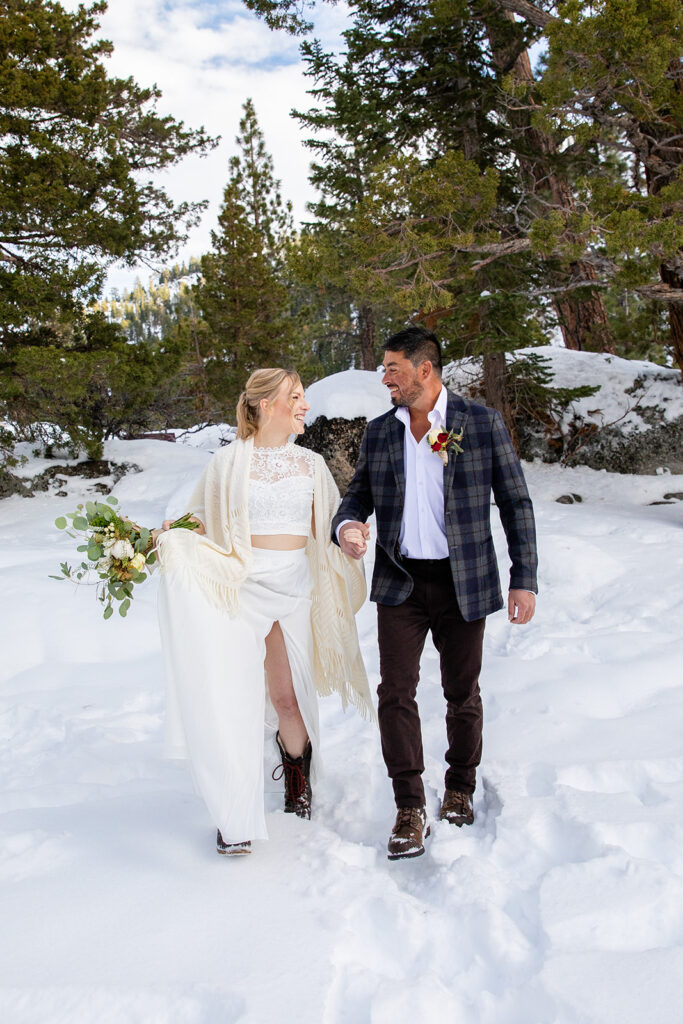 The bride and groom smile at each other while standing in deep snow among pine trees during their winter elopement in Lake Tahoe