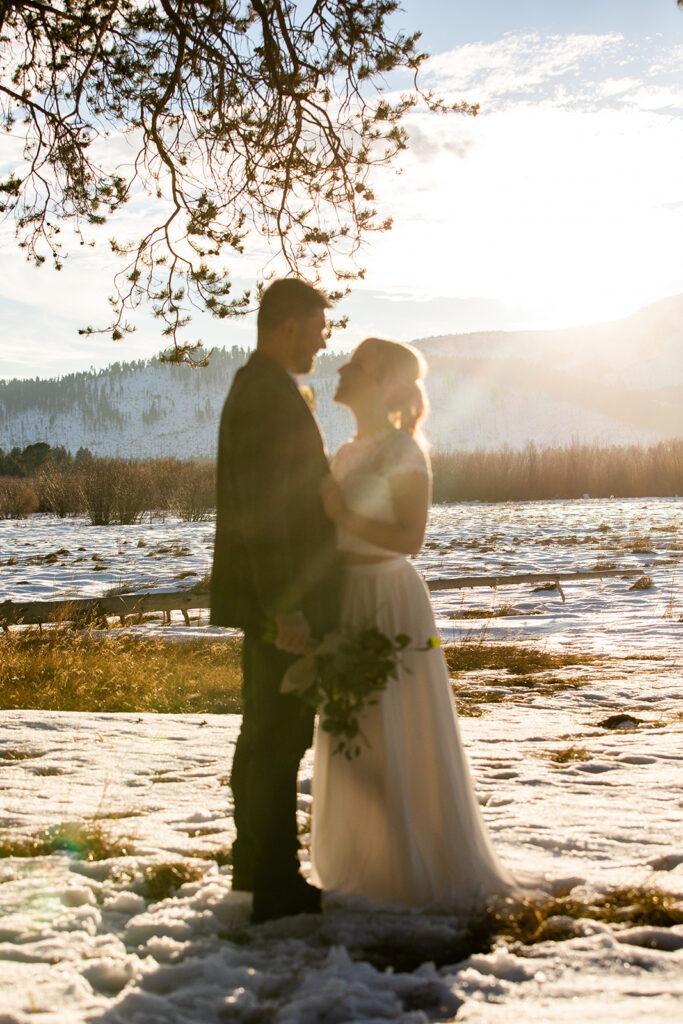 bride and groom in a snowy field kissed by golden hour light with mountains glowing in the background.