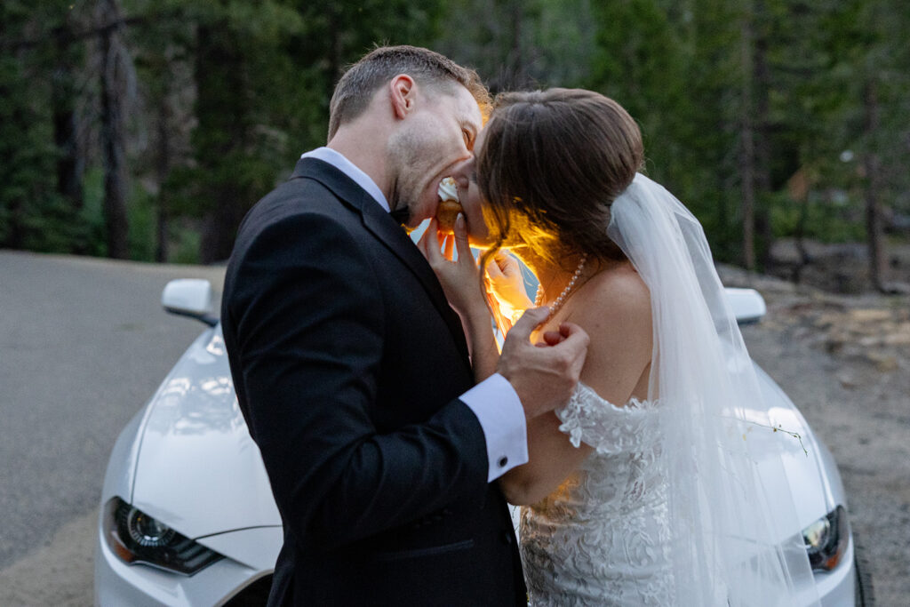 bride and groom sharing a cupcake in front of their wedding car