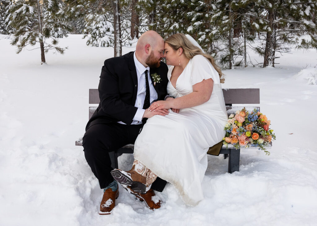 bride and groom sitting on a bench surrounded by snow during their snowy spring micro wedding in Lake Tahoe
