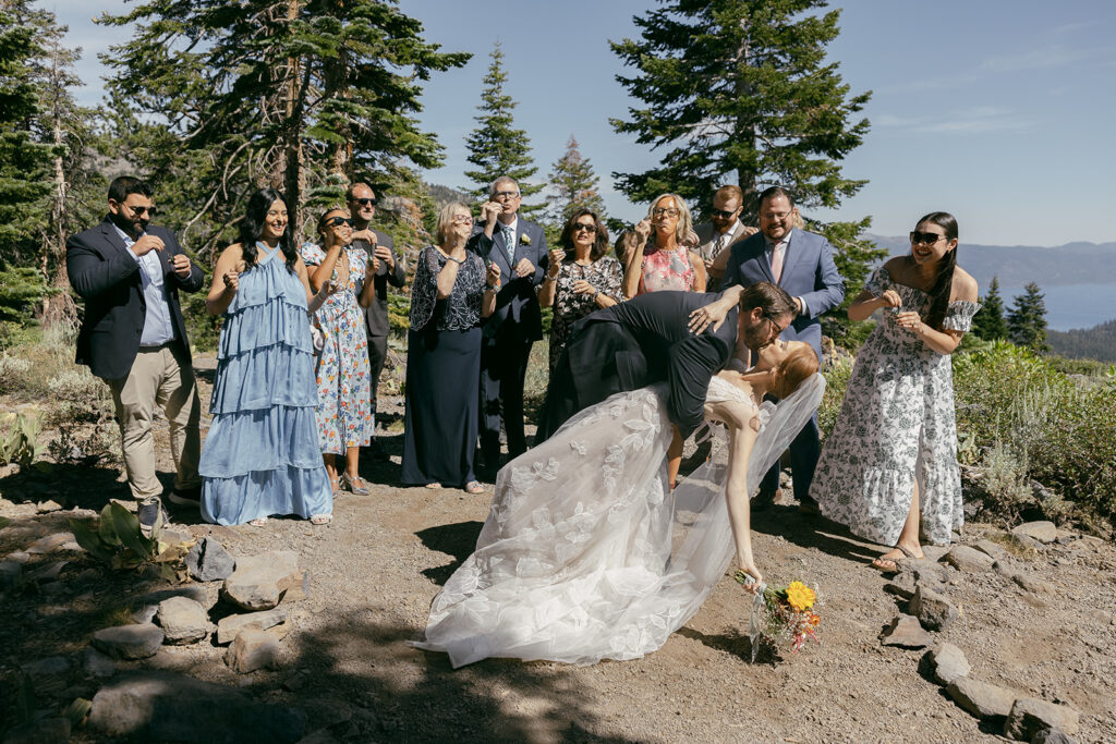 bride and groom dip kiss with family cheering them on